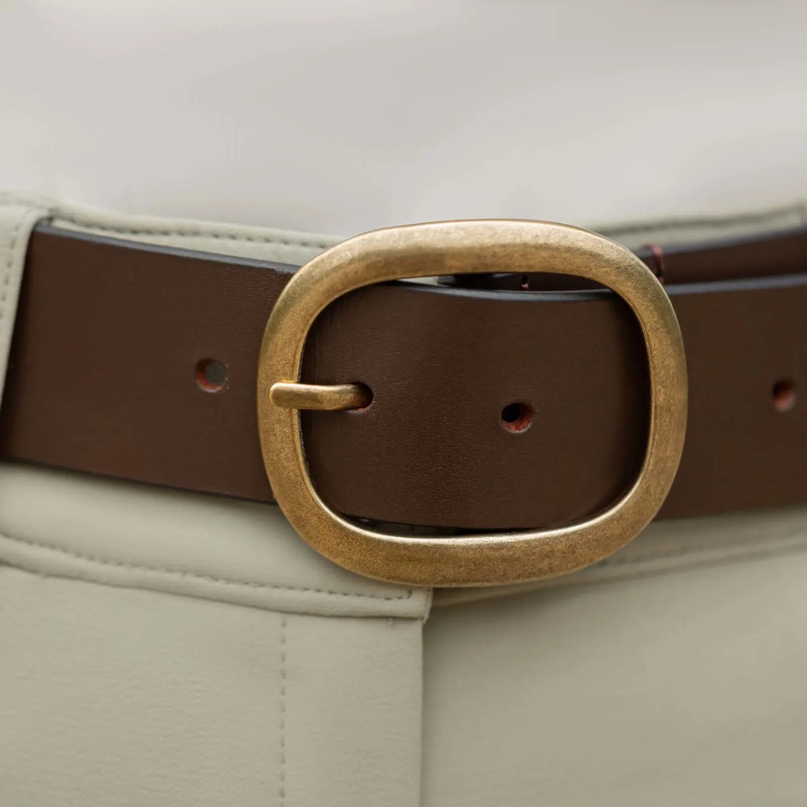 Close up view of the buckle of the Equinavia Emmi Flowers Leather Belt in chocolate brown worn over tan breeches
