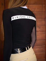 Back-view of a female model wearing the Criniere Estella Noir Night Long Sleeve Shirt with a wood plank background