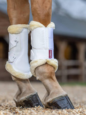 Horse wearing white LeMieux Fleece Edged Brushing Boots standing on gravel