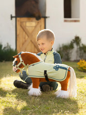 A young boy sitting outside next to a palomino stuffed animal horse