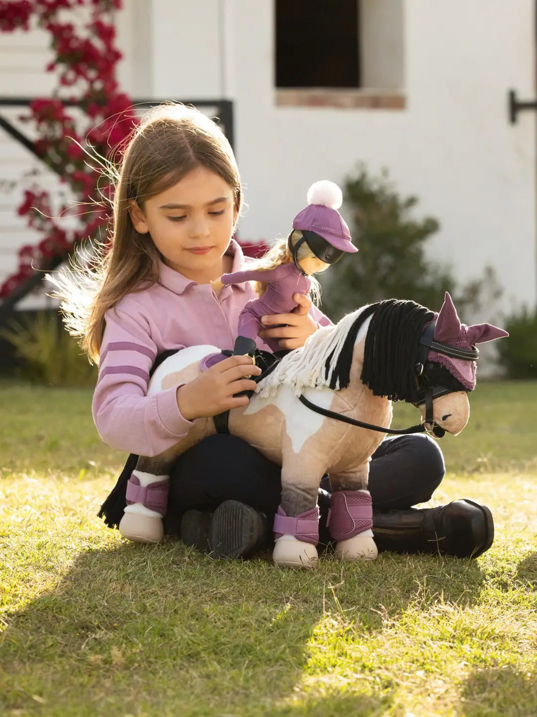 A young girl sitting outside with a buckskin pain stuffed animal horse - both dressed in purple