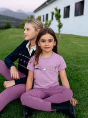 View of 2 young female models sitting outside in the grass and one of them is wearing the fondant LeMieux Mini Alex T-Shirt 