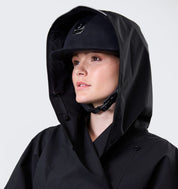 Close-up of model wearing Horseware H2O Poncho in black with hood up and riding helmet