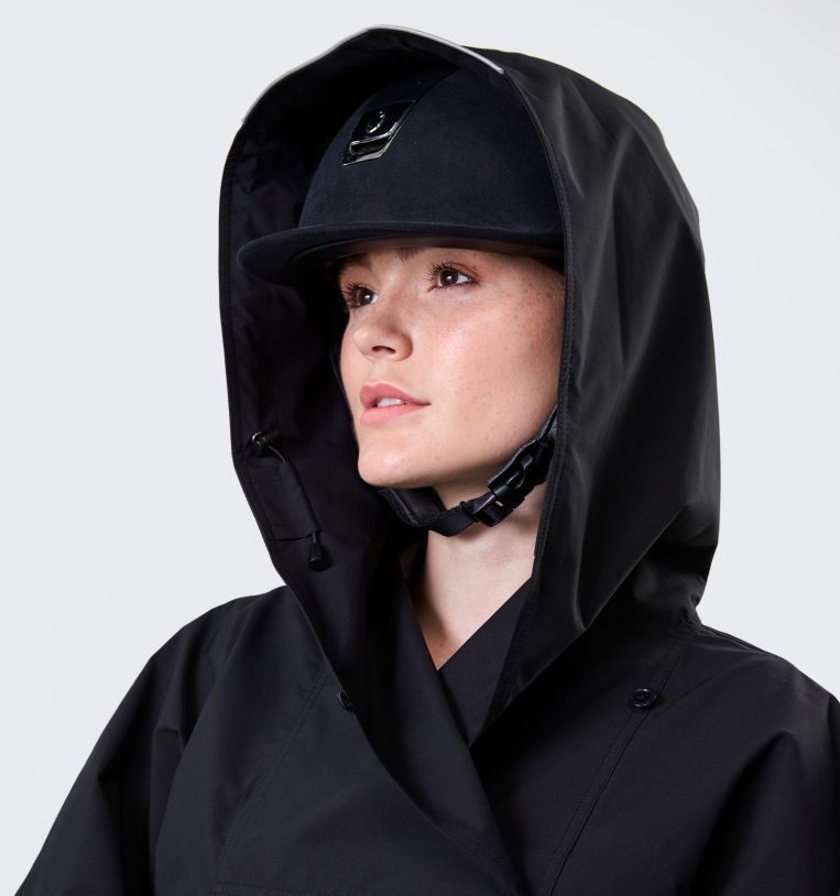 Close-up of model wearing Horseware H2O Poncho in black with hood up and riding helmet