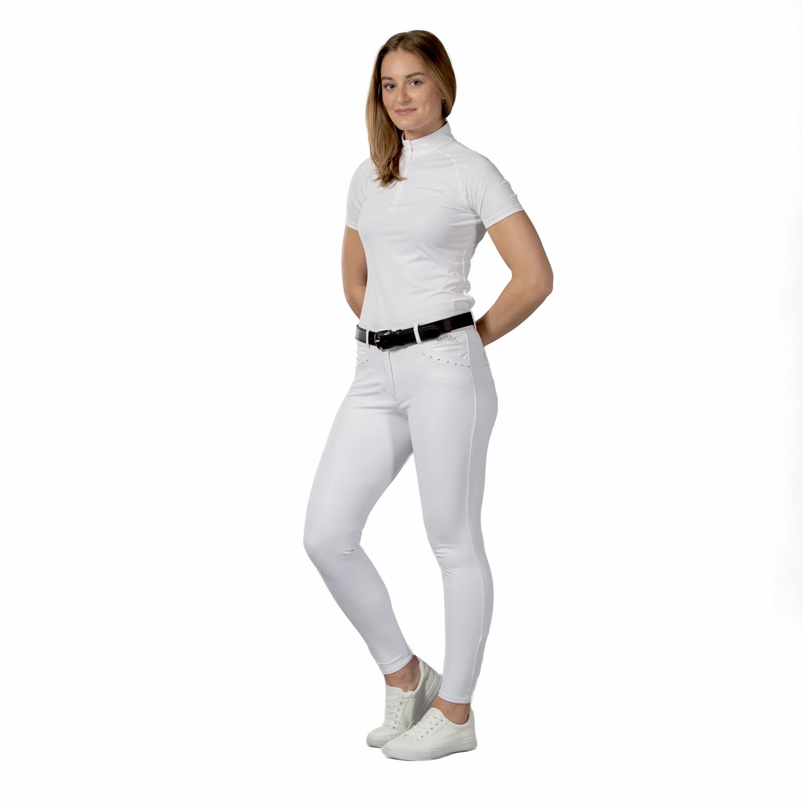 Full body front view of a model wearing the white Front view of a model wearing the white B Vertigo Olivia Sillicon Full Seat Breeches, white top, and white tennis shoes on a white background