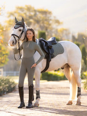 Full body front view of a young female model wearing the green Lemieux Young Rider Orla Pull On Tight and coordinating green top while standing in front of a white pony