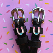 Close-up view of the Horse Shoe Party Mane Jane Spur Straps on a pink background with confetti sprinkles