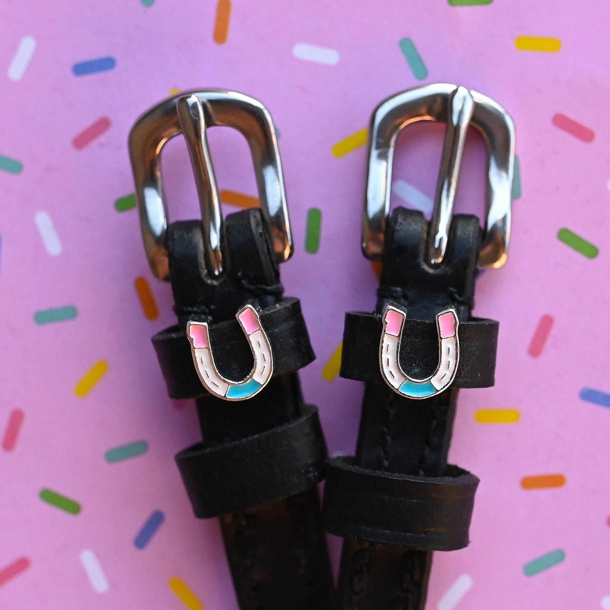 Close-up view of the Horse Shoe Party Mane Jane Spur Straps on a pink background with confetti sprinkles