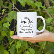 Front view of the Canary Road Horse Girl Coffee Mug with greenery in the background