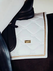 Close-up side view of the gold Side view of a female model riding a chestnut horse with a white Equestrian Stockholm White Perfection Dressage Pad