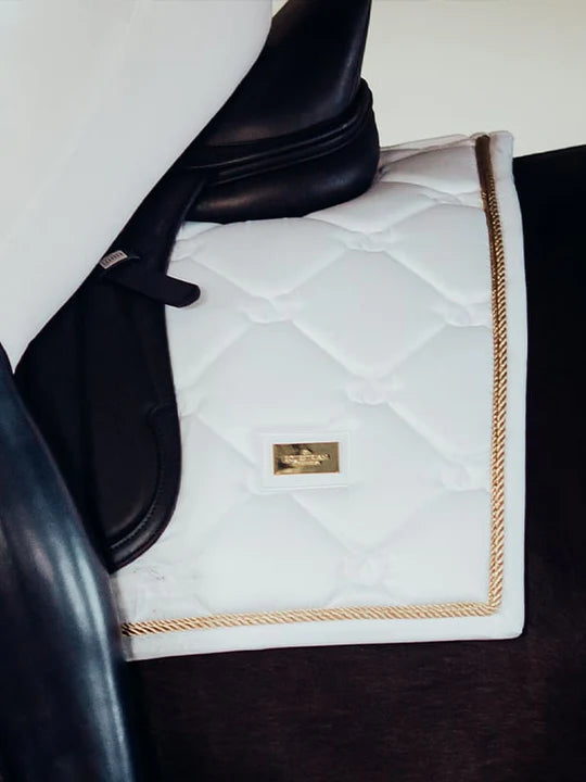 Close-up side view of the gold Side view of a female model riding a chestnut horse with a white Equestrian Stockholm White Perfection Dressage Pad