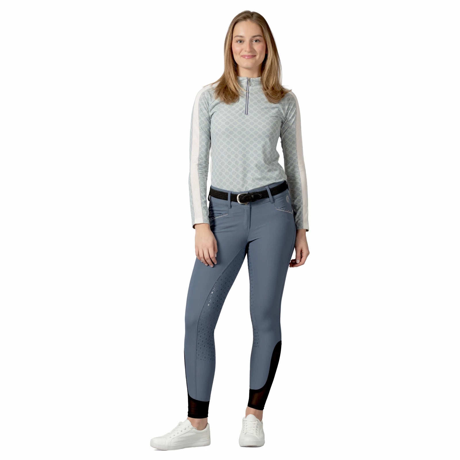 Full body front view of a female model wearing the blue Equinavia Victoria Full Seat Breeches and light blue long sleeve top on a white background