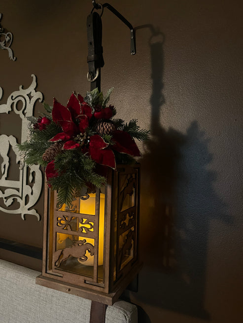 Side view of the jumping All Designs Equine Horse Lantern hanging on a brown wall with decorative christmas florals on the top of the lantern