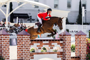 Side view of a male model using the Free Jump Soft'Up Pro+ Stirrups while riding a horse over a jump in an outdoor arena