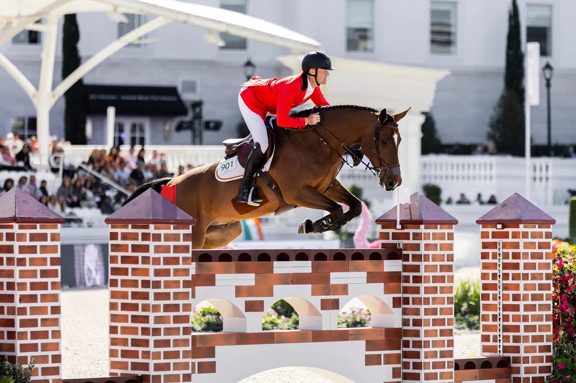 Side view of a male model using the Free Jump Soft'Up Pro+ Stirrups while riding a horse over a jump in an outdoor arena