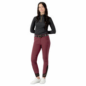 Full body front view of a model wearing the wine red Equinavia Maud Knee Patch Breeches, black top, and white tennis shoes on a white background