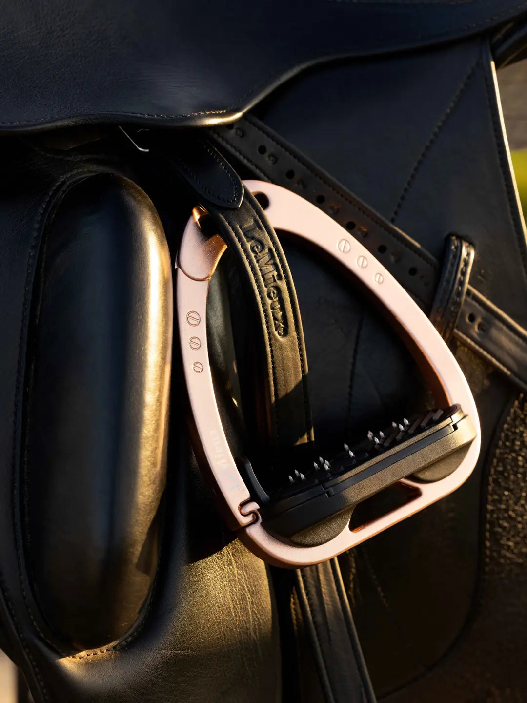 Front view of a rose gold LeMieux Vector Control Stirrup on a black dressage saddle