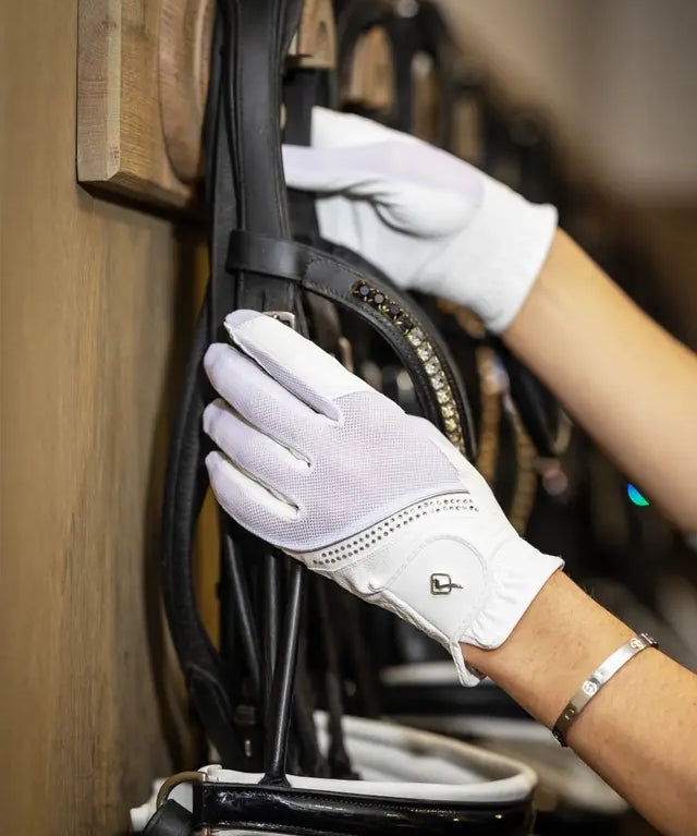 Person wearing white LeMieux Crystal Gloves while adjusting a bridle on a bridle rack
