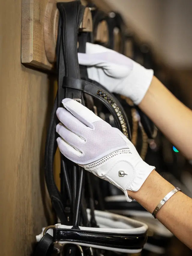Person wearing white LeMieux Crystal Gloves while adjusting a bridle on a bridle rack