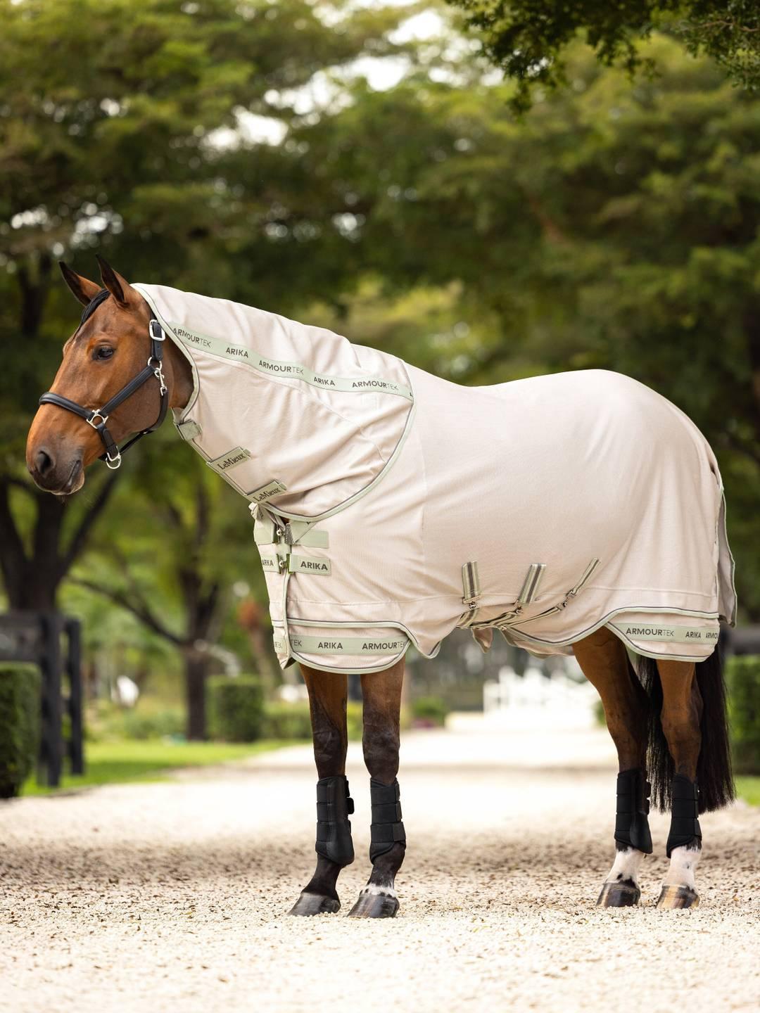 Side view of a bay horse wearing the stone LeMieux Arika Armour-Tek Fly Blanket while standing on a gravel path