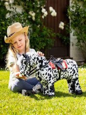 Side view of a young model playing outside with an appaloosa toy pony that is wearing the black LeMieux Toy Pony Western Bridle