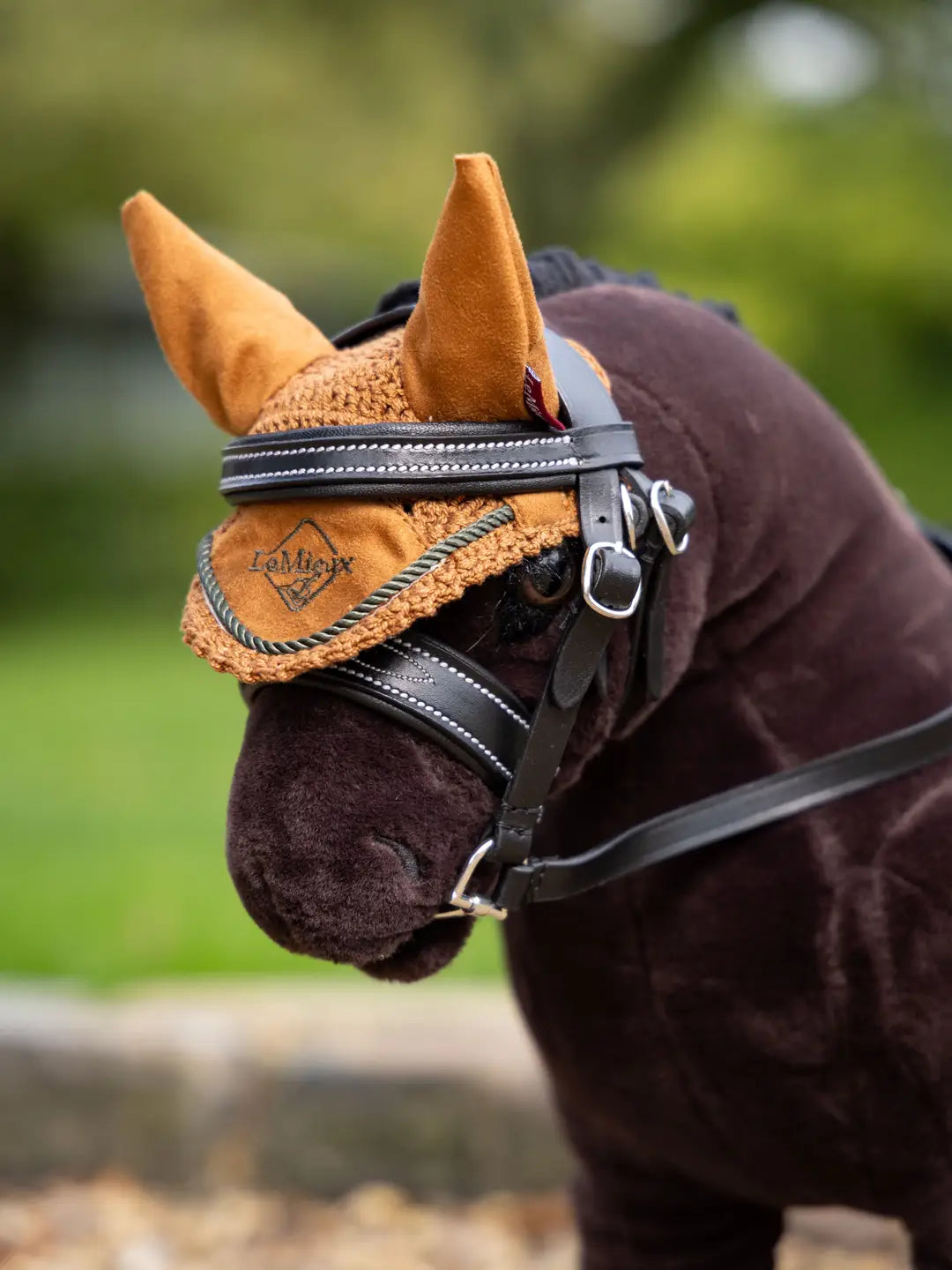 Close-up angled front view of a dark colored toy pony wearing the ginger LeMieux Toy Pony Fly Hood