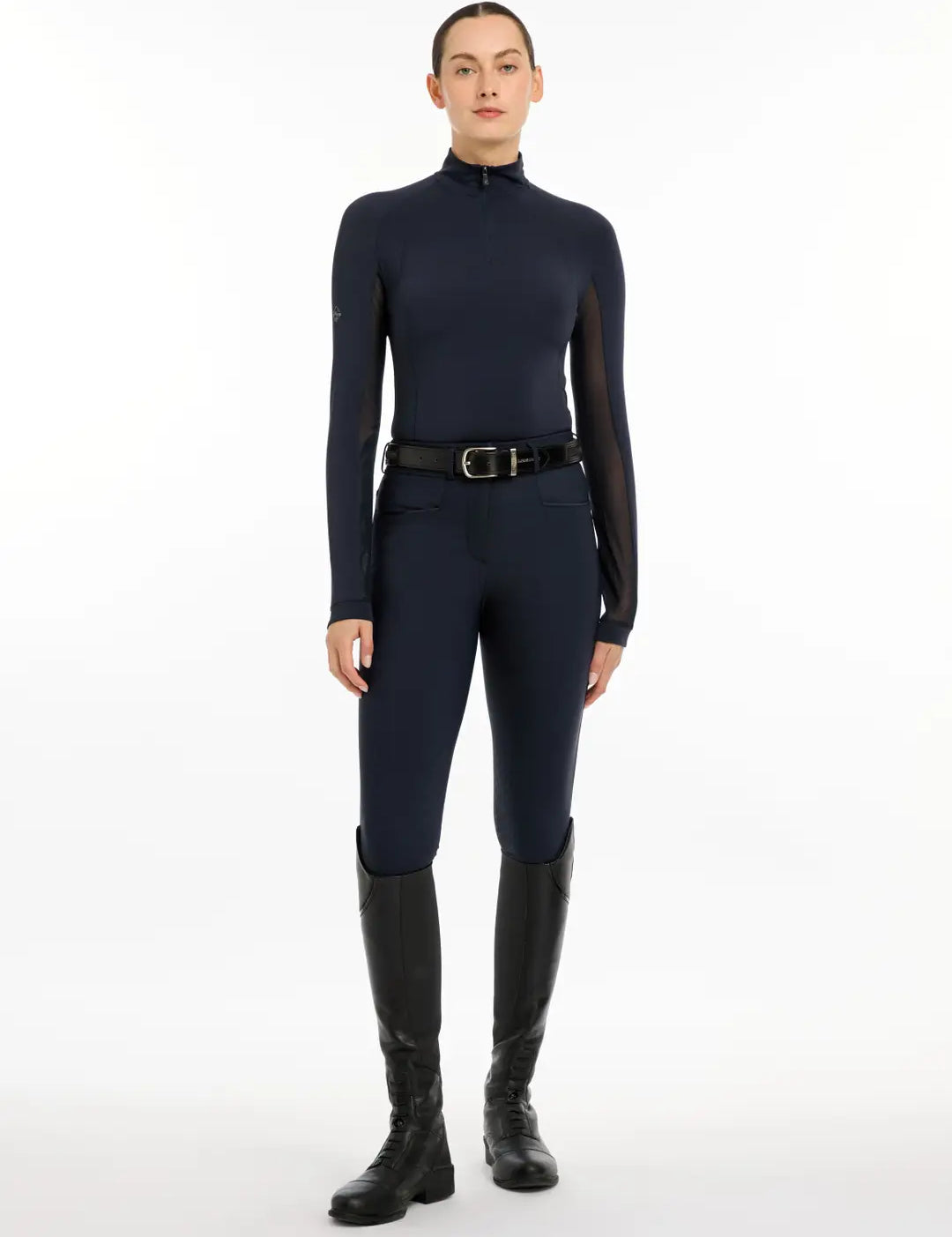Full body view of a model wearing the navy LeMieux Halle Lightweight Base Layer, navy breeches, and black tall boots on a white background