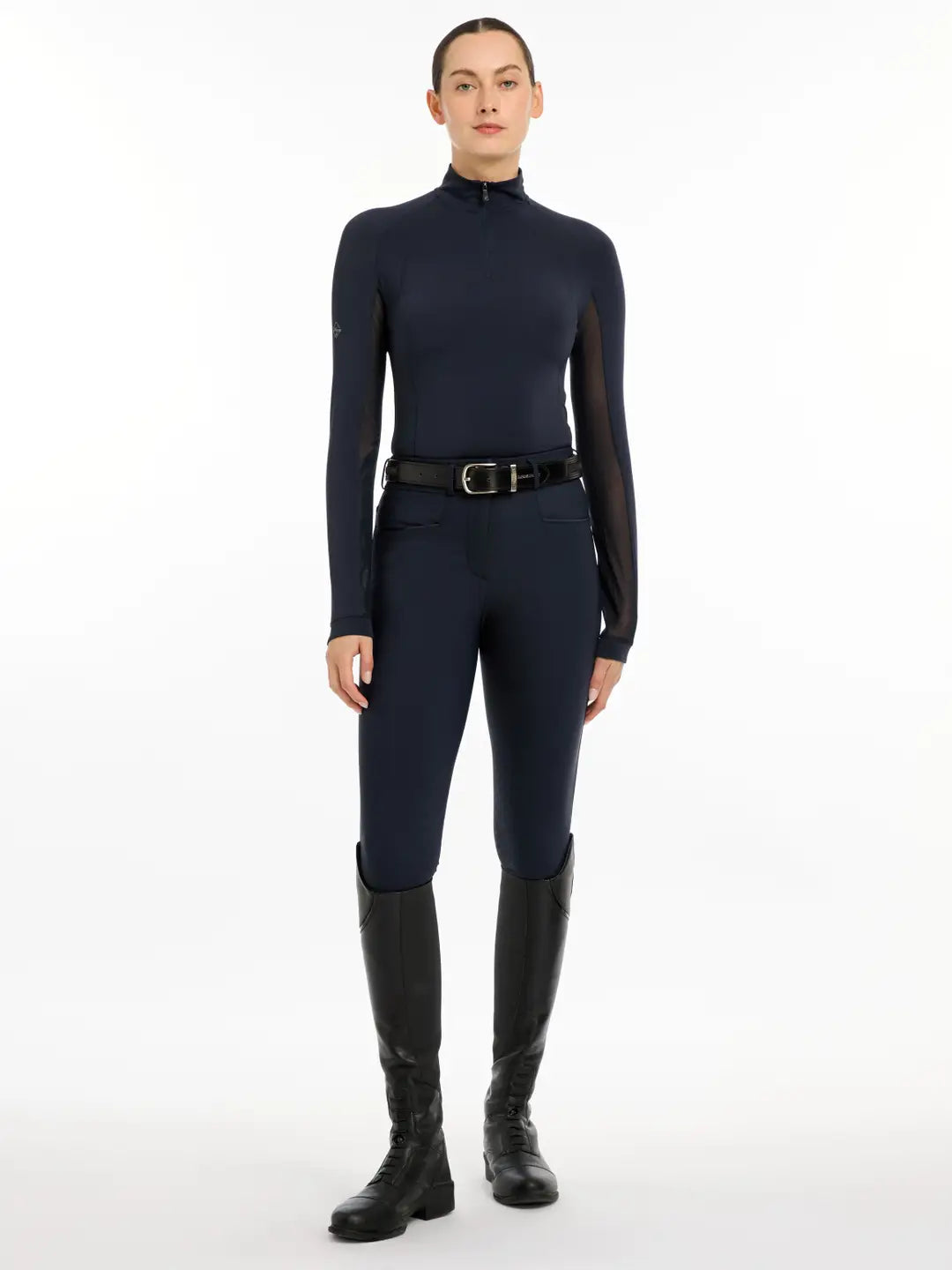 Full body view of a model wearing the navy LeMieux Halle Lightweight Base Layer, navy breeches, and black tall boots on a white background