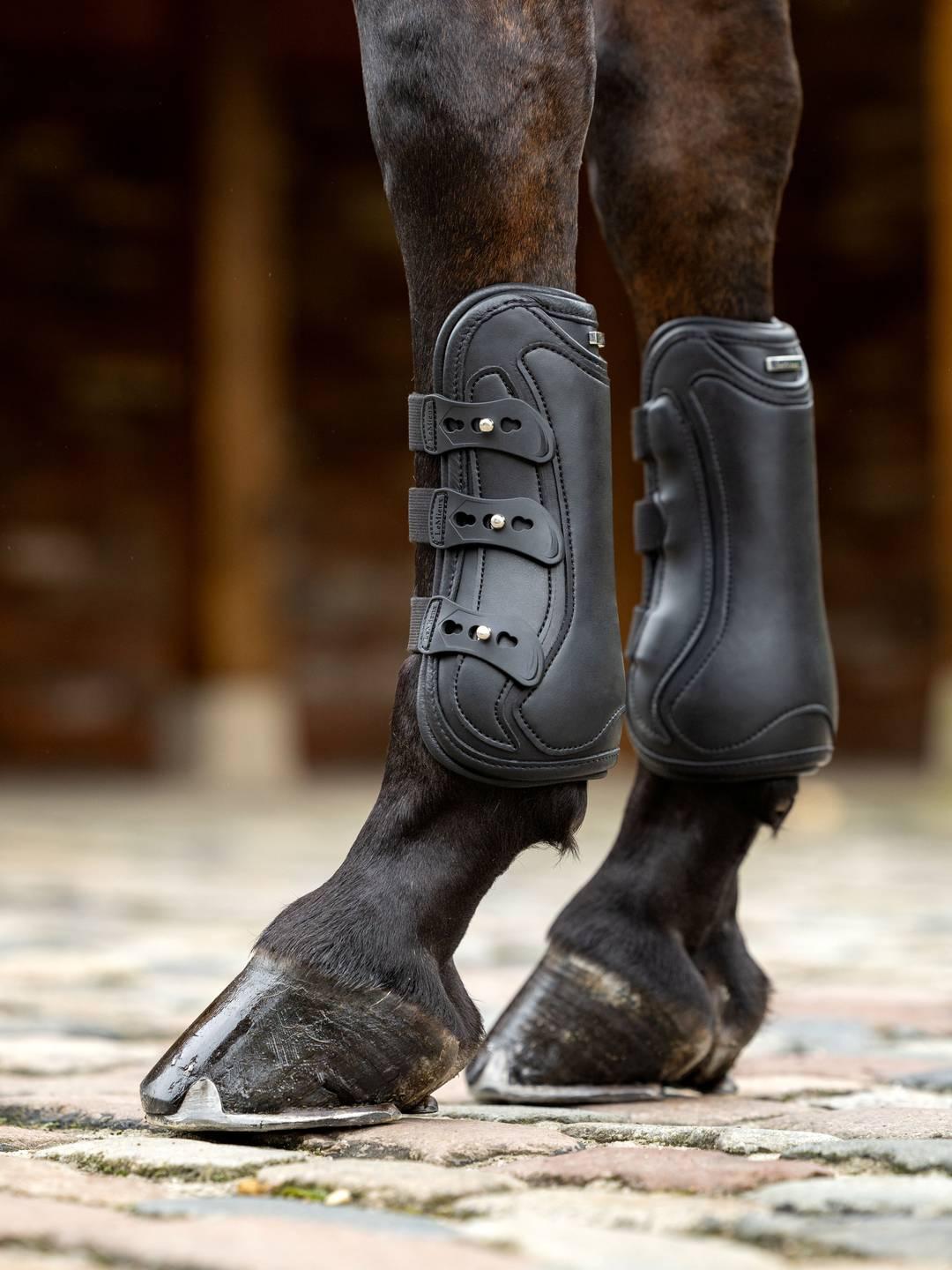 Close-up side view of a horse wearing a pair of black LeMieux Capella 3 Strap Tendon Boots while standing on a brick path