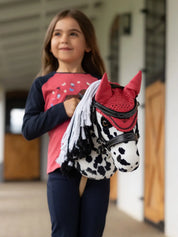 Front view of a young female model riding the Dakota Appaloosa LeMieux Hobby Horse in a barn aisle