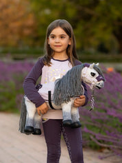 A young girl dressed in purple holding a gray stuffed animal horse dressed in purple