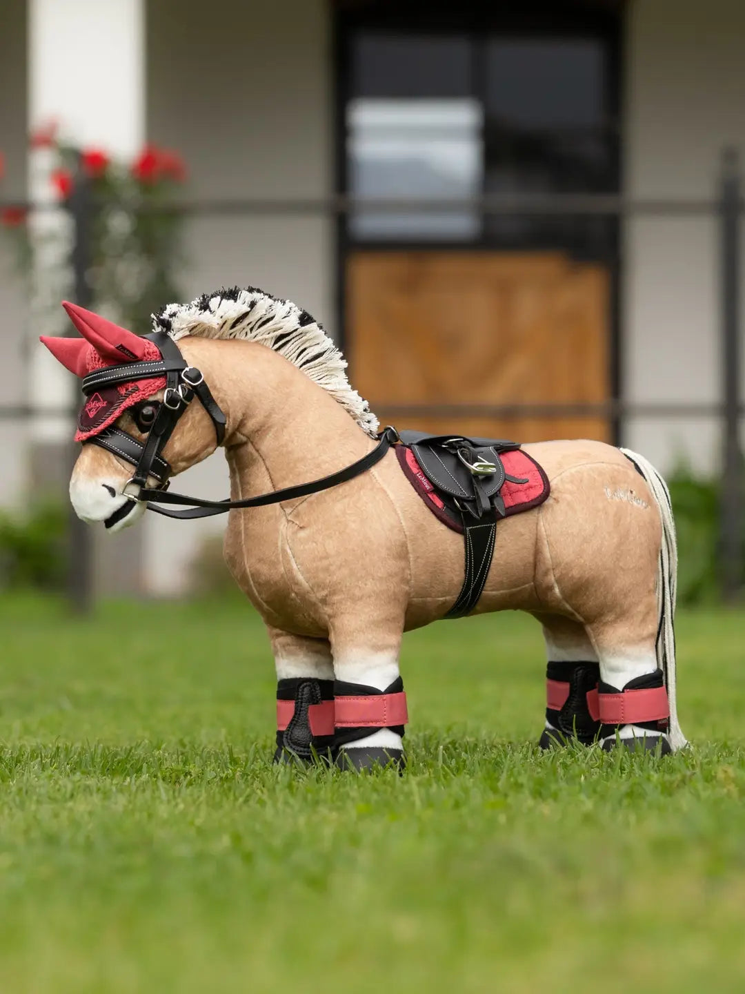 Side view of a fjord toy pony wearing the cranberry LeMieux Toy Pony Fly Hood and matching set while standing in the grass