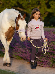 Front view of a child wearing the purple LeMieux Mini Romie Hoody while leading a paint pony outside