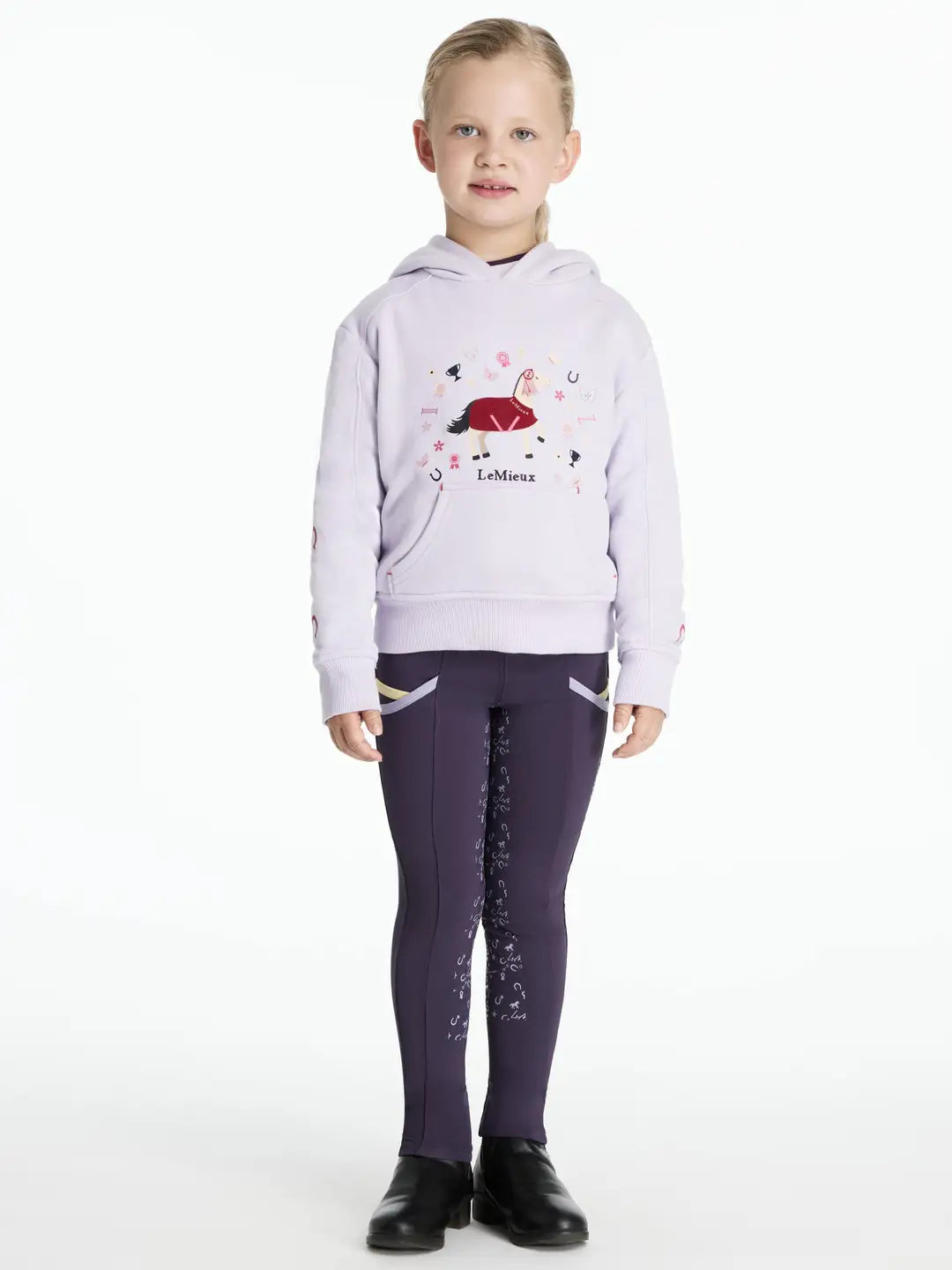 Full body front view of a young child wearing the purple LeMieux Mini Romie Hoody, purple breeches, and black boots on a white background