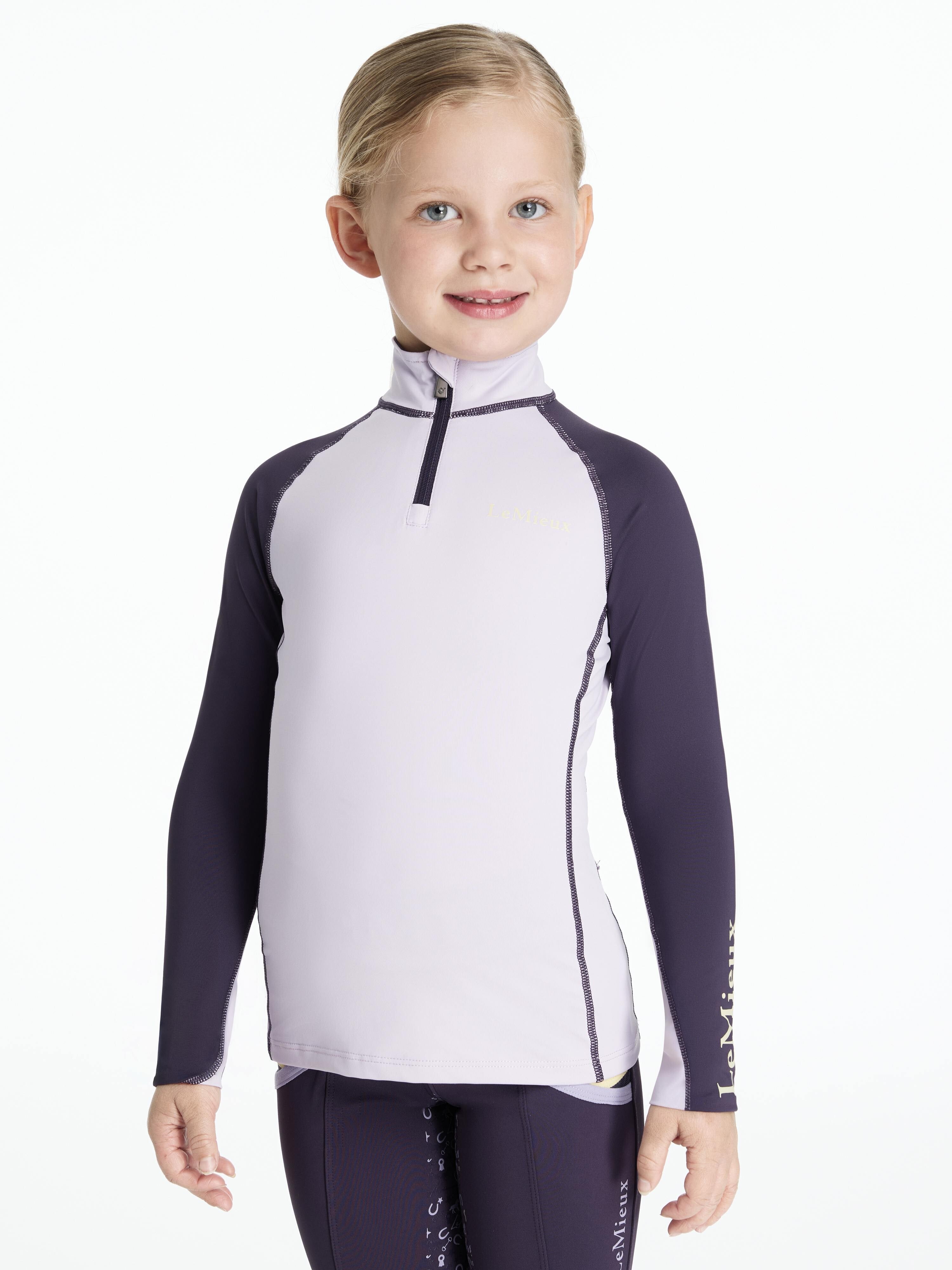 Front view of a young female model wearing the purple LeMieux Mini Long Sleeve Baselayer on a white background