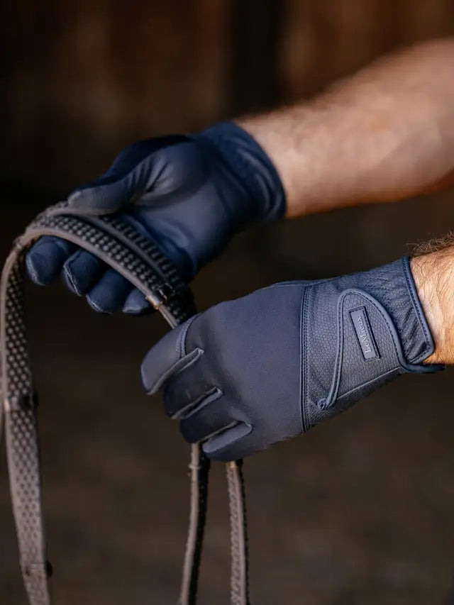 Person wearing dark blue gloves holding a horse bridle against a blurred background
