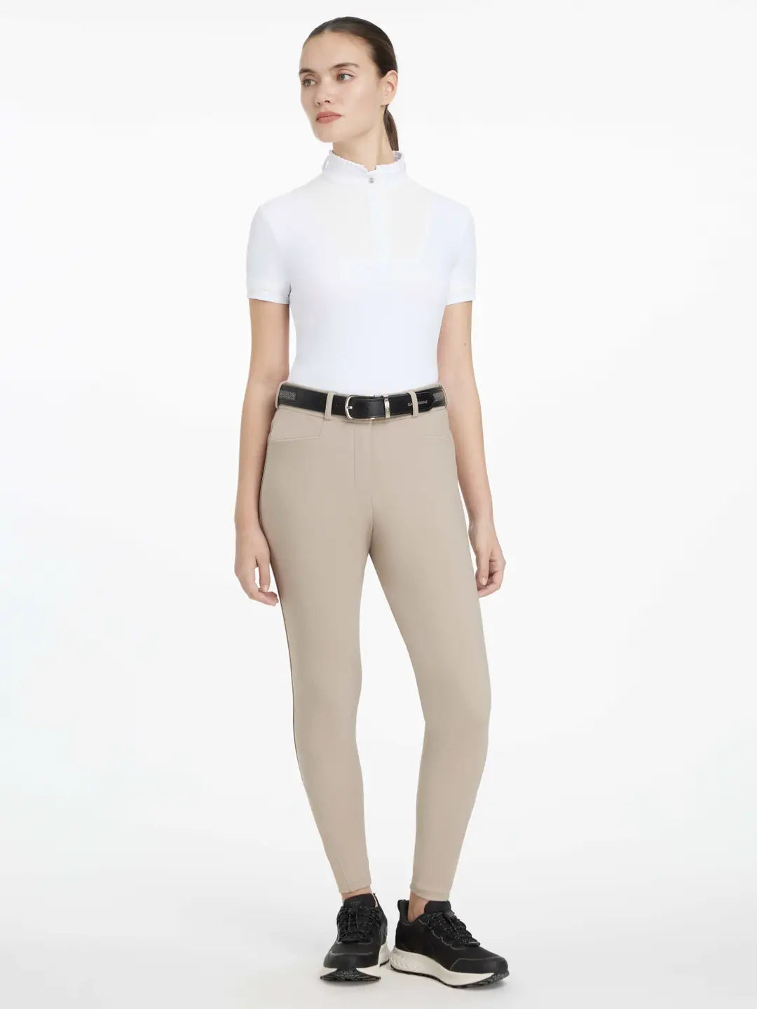 Full body front view of a model wearing the tan LeMieux Isabelle Knee Grip Breeches and white shirt on a white background