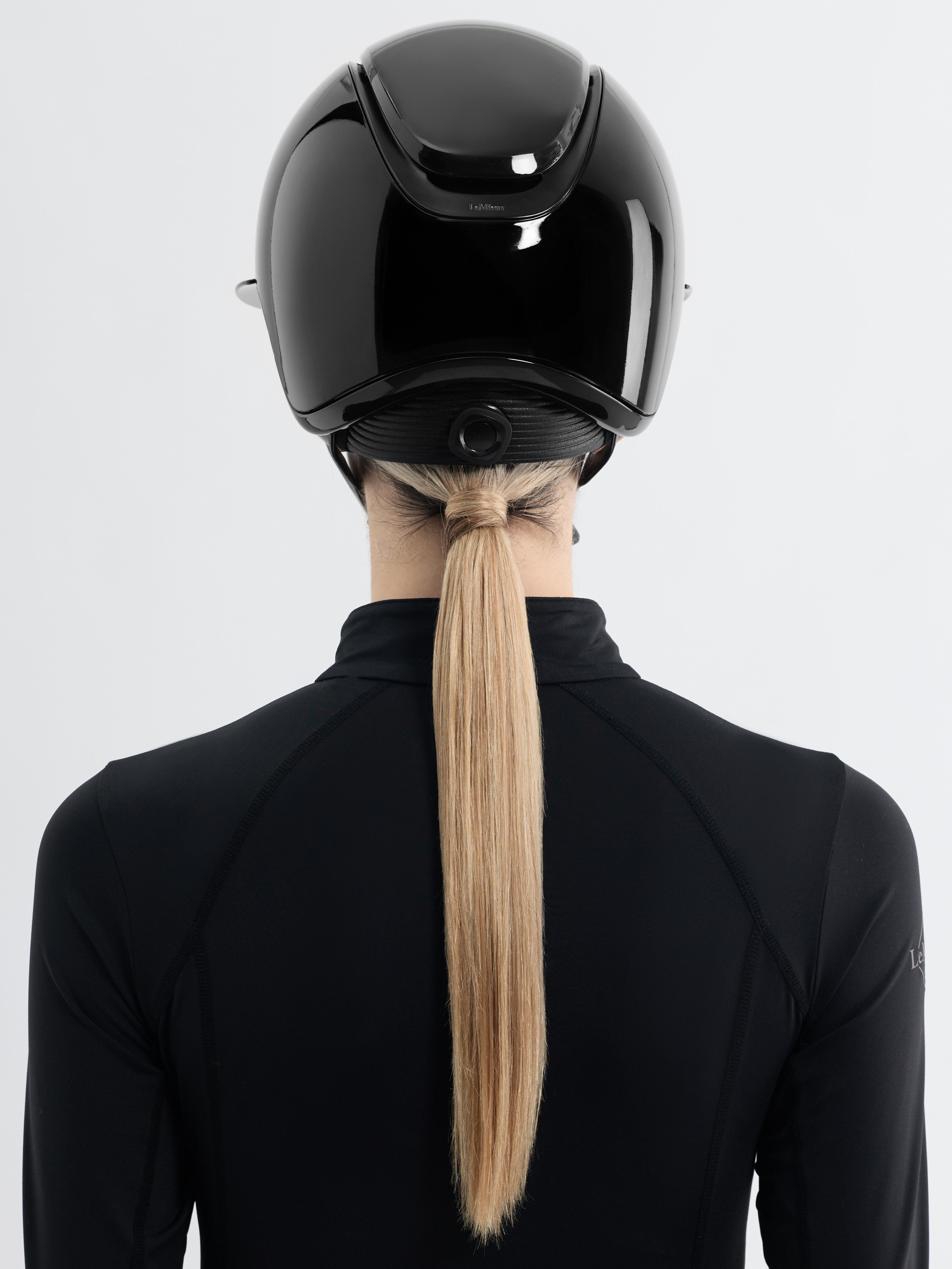 Back view of a female model wearing the black LeMieux Verv® Competition Gloss Helmet on a plain background