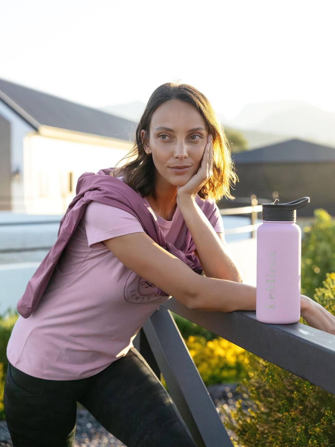 View of the fondant LeMieux Drinks Bottle set on a railing with a model leaning on the railing behind it