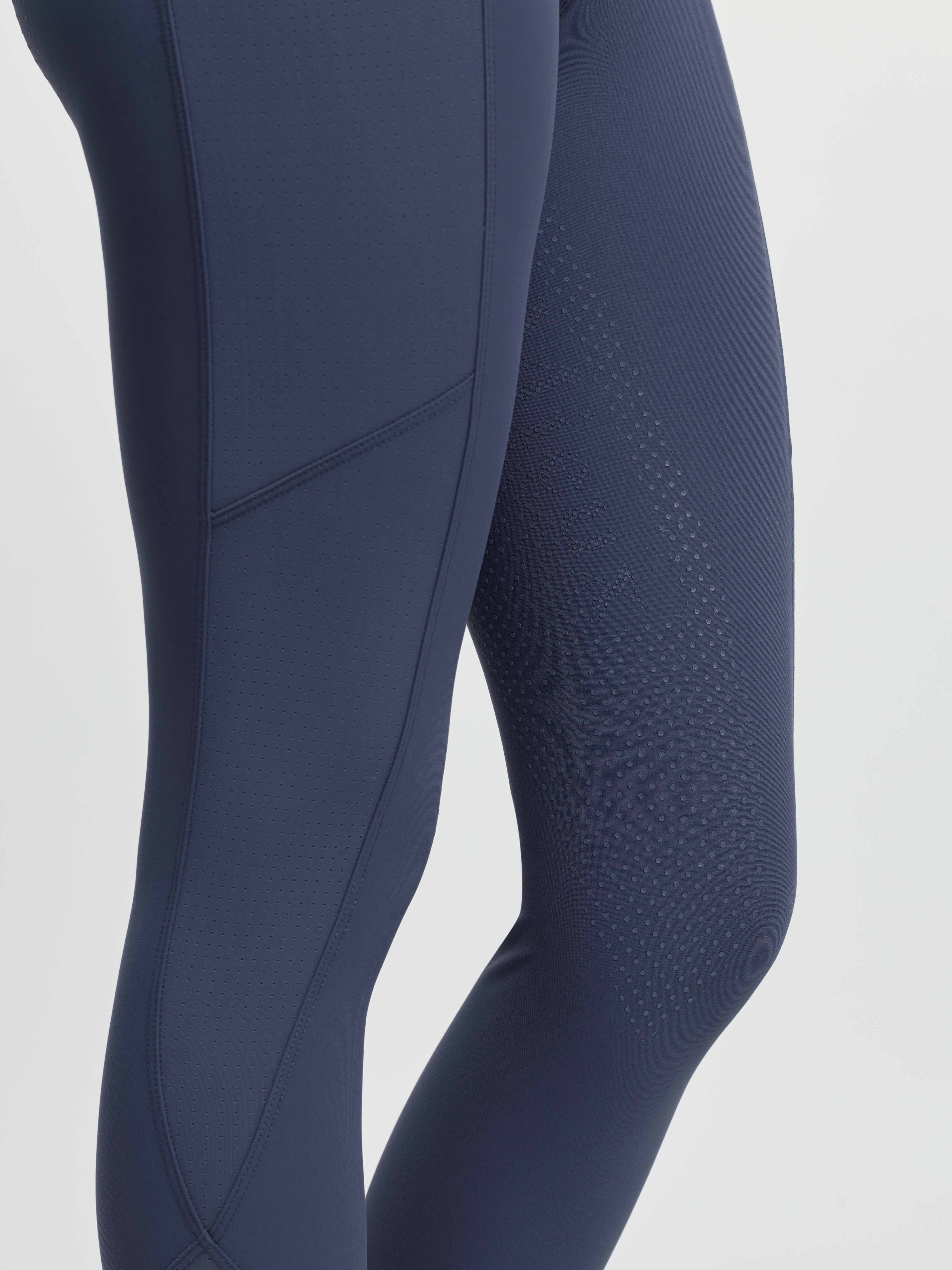 Close-up side view of a model wearing the blue LeMieux Airflow Full Seat Pull On Breeches on a plain background