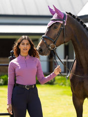 Front view of a female model wearing the purple LeMieux Airflow Long Sleeve Base Layer while standing next to a horse
