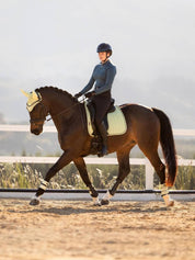 Side view of a model riding a horse that is wearing the macaron LeMieux Suede Dressage Square Pad