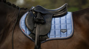 Close-up of light blue saddle pad under a black saddle on a horse