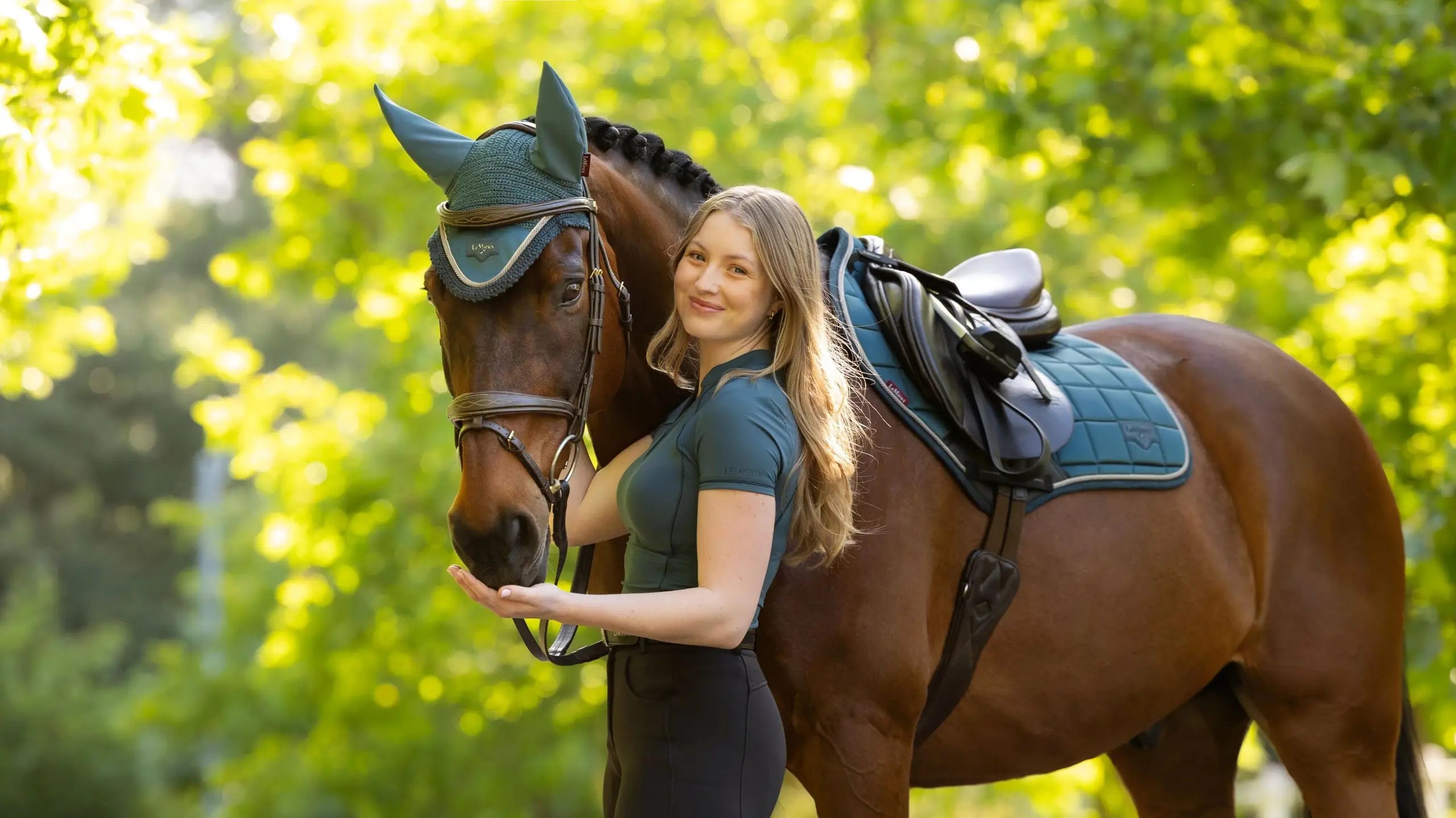 Person standing beside a horse wearing a green saddle pad