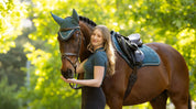 Person standing beside a horse wearing a green saddle pad