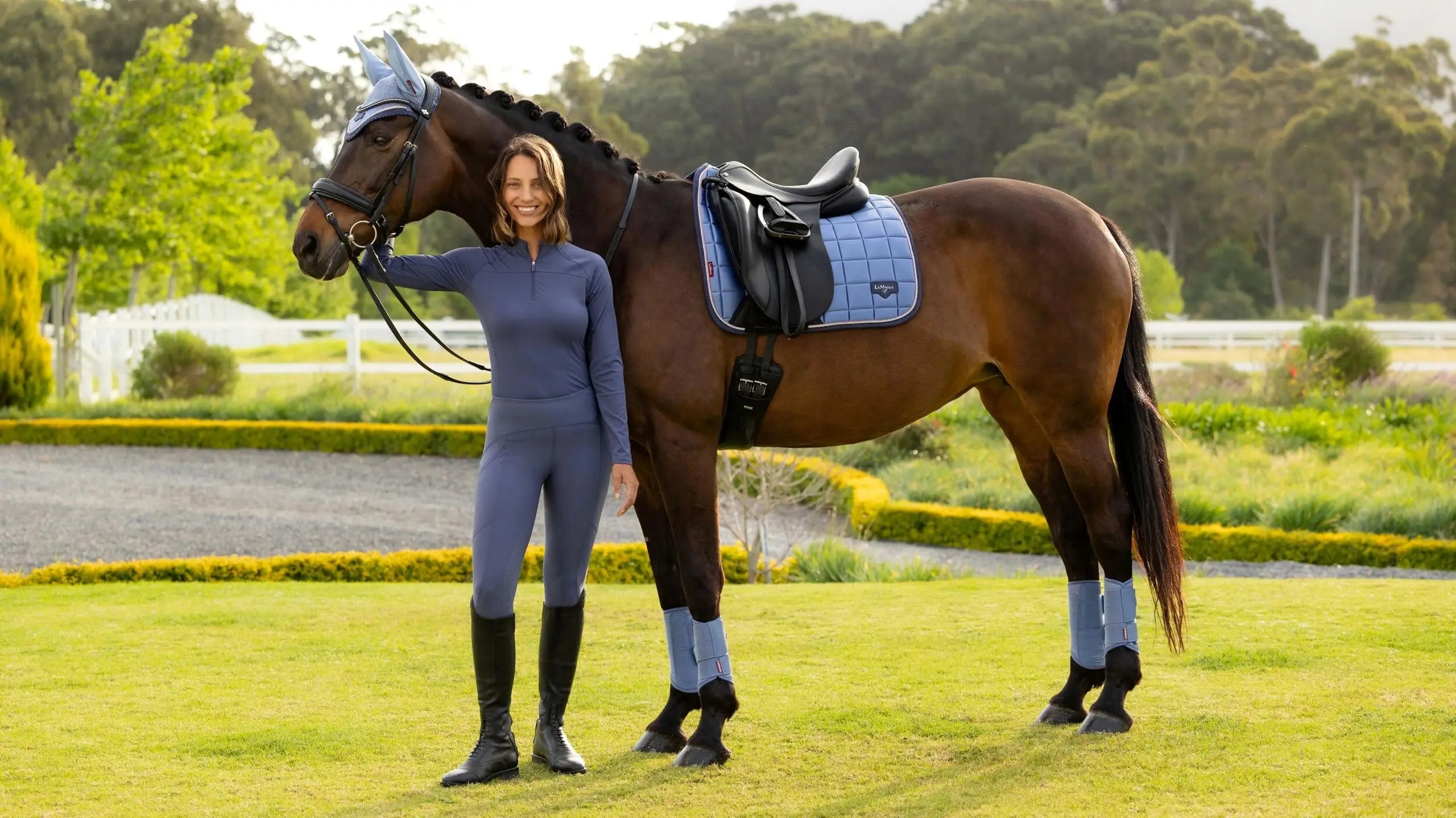 Person standing beside a horse wearing a light blue dressage saddle pad