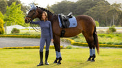 Person standing beside a horse wearing a light blue dressage saddle pad