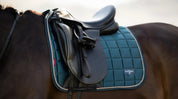 Close-up of green quilted dressage saddle pad under a black saddle on a horse