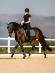 Woman riding horse in outdoor sand arena with LeMieux Jungle saddle pad and accessories