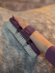 Close up view of a woman grooming a gray horse with the Lemieux Flexi Goats Hair Body Brush in purple and light blue with cream colored bristles